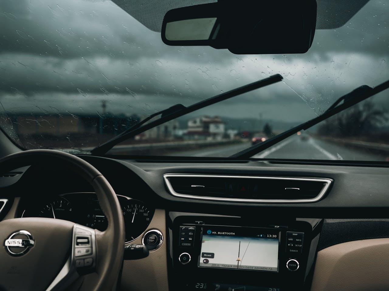 Interior view of a car on a rainy road, capturing steering wheel and dashboard.